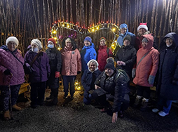 Group of Trefoil Guilds pose for picture in front of seasonal light display